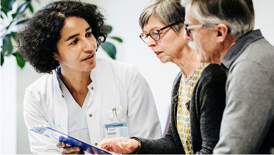Clinician meeting with two adults at a desk.