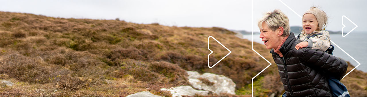 Person carrying child on their back, while walking at the beach.