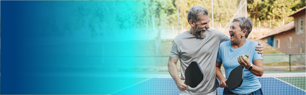 Two people smiling while holding pickleball paddles.
