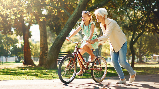 Child riding a bicycle with adult guiding alongside in a sunny park.