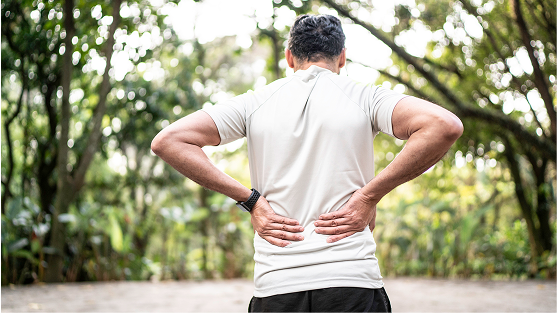 Person outdoors holding lower back in discomfort.